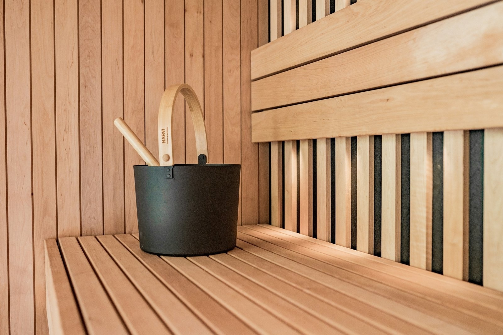 Sauna bench with backrest slats, wooden bucket and ladle in a Berkeley build