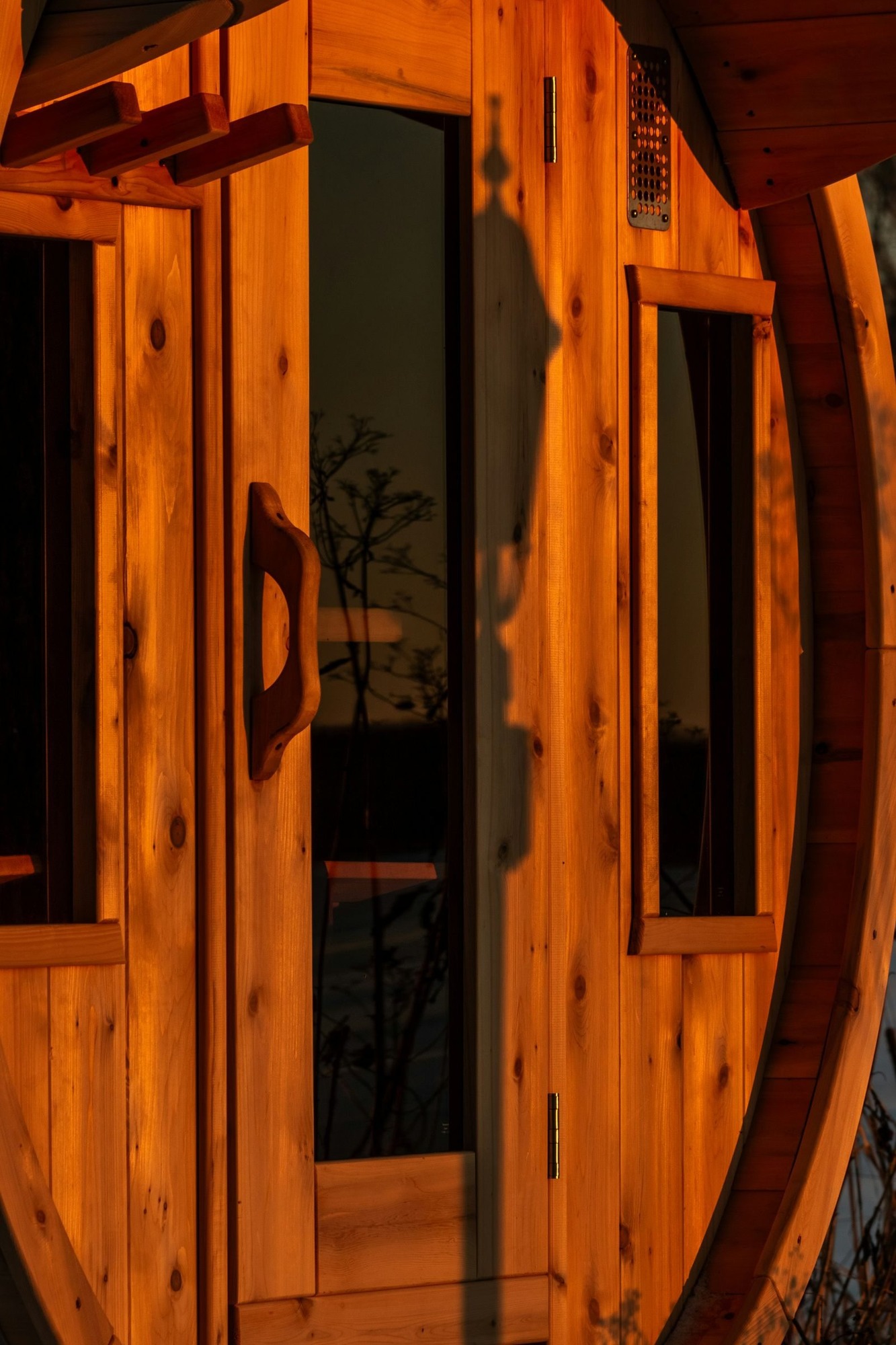 Cedar door with glass panes on a barrel sauna end wall, built by our Berkeley crew